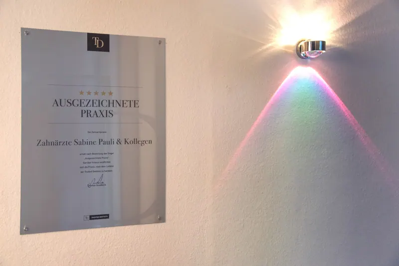 Auszeichnung „Ausgezeichnete Praxis“ an der Wand neben einer Wandlampe
