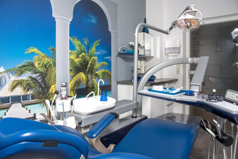 Behandlungszimmer mit blauem Zahnarztstuhl und Wandbild mit Meerblick