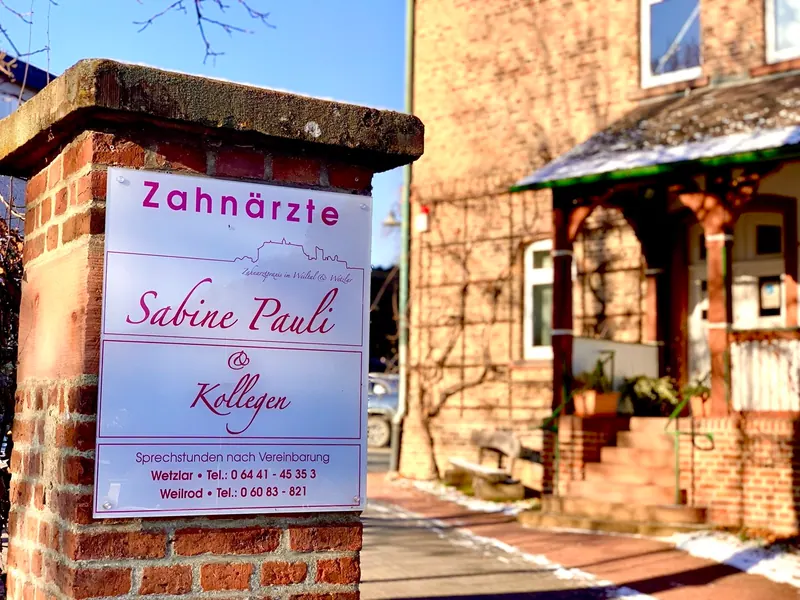 Eingang der Zahnarztpraxis mit Praxisschild an einer Backsteinmauer